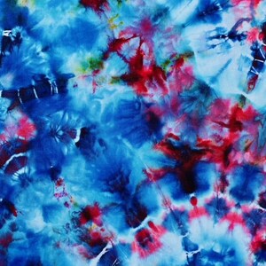 May include: Abstract tie-dye pattern in shades of blue, red, and white. The design features a swirling, cloud-like effect with bursts of colour. The fabric has a soft, textured appearance, suggesting a comfortable material.