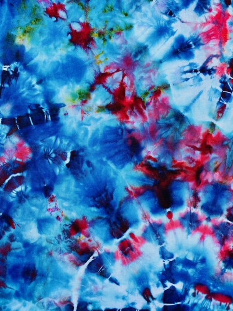 May include: Abstract tie-dye pattern in shades of blue, red, and white. The design features a swirling, cloud-like effect with bursts of colour. The fabric has a soft, textured appearance, suggesting a comfortable material.