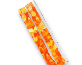 May include: A pair of long, orange and white tie-dye socks. The socks are laid out flat on a white surface with a measuring tape beside them.