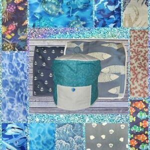 May include: A collage of marine-themed fabrics and items. The central focus is a teal beanbag chair with a white pocket. Surrounding it are fabric swatches with sea turtles, fish, anchors, and coral patterns in shades of blue and white.