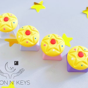 May include: Four yellow star-shaped keycaps with red and blue accents, arranged on different colored bases. The keycaps are decorated with small dots. The image also includes yellow star-shaped decorations and the Moon N' Keys logo.