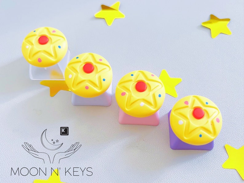 May include: Four yellow star-shaped keycaps with red and blue accents, arranged on different colored bases. The keycaps are decorated with small dots. The image also includes yellow star-shaped decorations and the Moon N' Keys logo.
