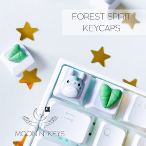 May include: White keyboard with green and white keycaps featuring a leaf design, a white keycap with a cartoon animal, and the text "FOREST SPIRIT KEYCAPS".