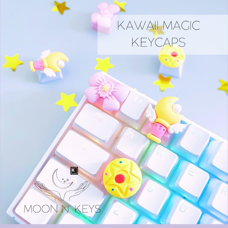 May include: A white keyboard with custom keycaps featuring kawaii designs. The keycaps include a yellow star, a pink flower, and a yellow character with wings. The text "KAWAII MAGIC KEYCAPS" is displayed.
