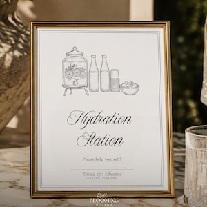 May include: A gold-framed sign with a white background featuring a black line drawing of a beverage dispenser, two bottles, a stack of cups, and a bowl. The text reads Hydration Station, Please help yourself!, Olivia & Thomas, ANY CITY, 17.08.2026.