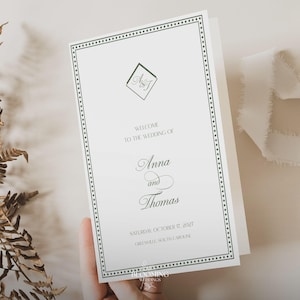 May include: A wedding program with a green border and text. The program reads "Welcome to the Wedding of Anna and Thomas" with the date and location. The program is held by a hand.