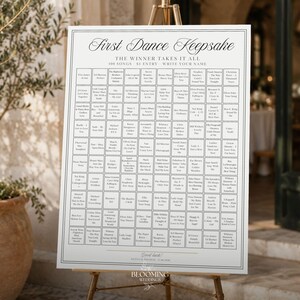 May include: A white rectangular sign titled First Dance Keepsake with the subtitle The Winner Takes It All. The sign features a grid of 100 squares, each containing a song title and artist name, with space for guests to write their names.