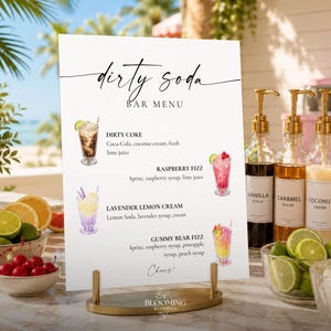 May include: A white rectangular bar menu sign with black text reading Dirty Soda Bar Menu, listing four drink options with illustrations, supported by a gold metal stand. The menu includes Dirty Coke, Raspberry Fizz, Lavender Lemon Cream, and Gummy Bear Fizz.