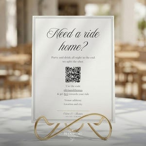Puede incluir: Un letrero rectangular blanco con un borde negro fino, exhibido en un soporte de metal dorado. El texto dice: Need a ride home? Party and drink all night in the end we split the uber. Incluye un código QR, el código oliviaandthomas y la dirección.
