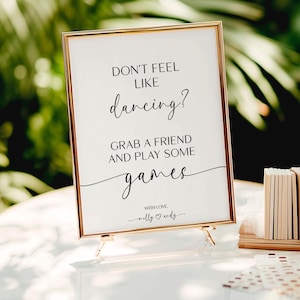 May include: A gold-framed sign with the text "Don't feel like dancing? Grab a friend and play some games. With love, Molly & Endy".