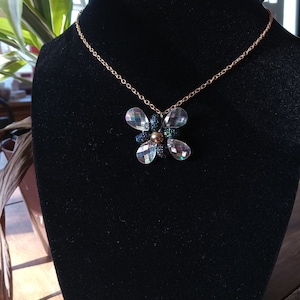 May include: A gold chain necklace with a clear crystal flower pendant. The flower has a black centre and iridescent facets.