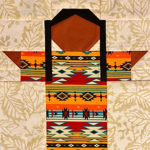 Puede incluir: Un bloque de colcha colorido que presenta a una persona estilizada con un patrón geométrico en su ropa. La persona tiene una cara marrón oscura y cabello negro. El fondo es beige claro con un patrón de hojas.