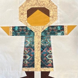 May include: A patchwork quilt block featuring a stylized person wearing a hooded coat with a patterned design. The person is standing on a white background.