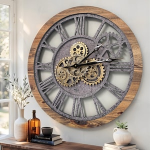 Puede incluir: Un gran reloj de pared redondo con marco de madera natural, esfera de metal gris texturizado con grandes números romanos y un grupo central de engranajes mecánicos dorados expuestos. El reloj tiene dos manecillas negras que marcan la hora.