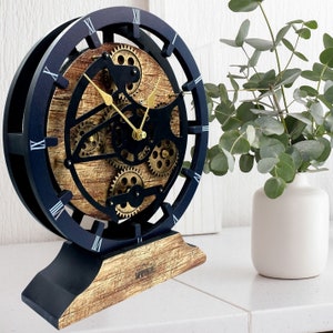 May include: A black and gold clock with a wooden base and exposed gears. The clock face has Roman numerals and a black background.