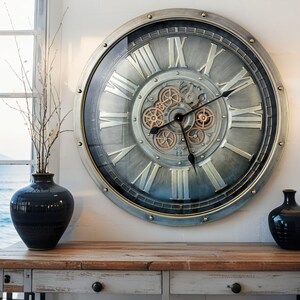 May include: Large, round wall clock with a silver and bronze finish. The clock features Roman numerals, visible gears, and black clock hands. The clock is mounted on a white wall above a wooden table, with a vase and decorative branches to the left.