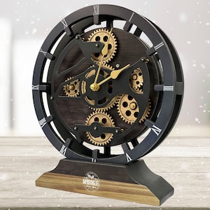 May include: Black and gold clock with a decorative gear design. The clock has Roman numerals and a black base with the words "Improving Life" printed on it.