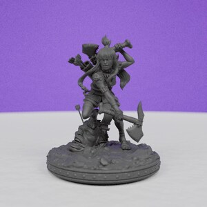 May include: A gray miniature figurine of a female warrior wielding a pickaxe and a bow and arrow. The warrior stands atop a sculpted base with a grotesque face. The figure is detailed with armor and flowing hair, suggesting a fantasy theme.