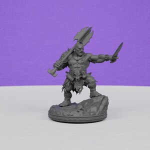 May include: A gray figurine of a muscular warrior, holding a large axe over his shoulder and a knife in his other hand. The warrior stands on a rocky base, with a detailed design on the base's edge. The background is a solid purple.