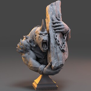 May include: A gray, sculpted bust of a monstrous creature with a horn on its head, holding a large, gray rock with a chain attached. The creature has a fierce expression and is wearing a spiked collar. The bust is mounted on a gold-colored base.