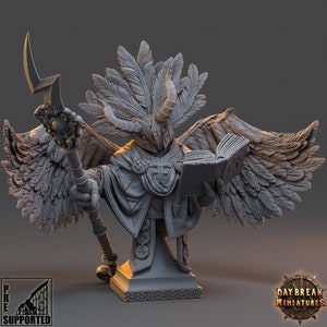May include: A gray, detailed miniature bust of a winged creature with a feathered headdress, holding a book and a staff. The creature has a horned mask and is wearing a robe with a cross design. The bust is on a square base with intricate details.