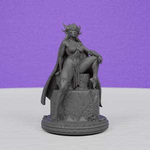 May include: A gray figurine of a woman with a horned headdress and a flowing cape, seated on a stone pedestal. The statue is detailed with intricate designs and textures, showcasing a fantasy theme.