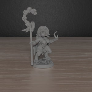 May include: A grey, detailed miniature figurine of a female lizard person holding a staff with a curved top and a small flame in her other hand. She is wearing a headdress and a skirt with a decorative pattern.