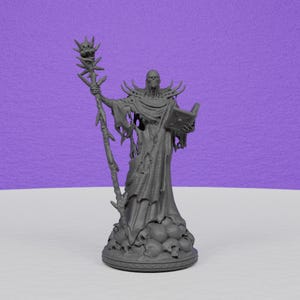 May include: A gray figurine of a robed figure holding a staff and a book. The figure has a skeletal face and is standing on a base with skulls. The staff has a skull at the top. The background is purple.