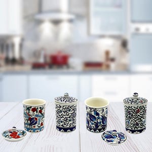 May include: Set of four ceramic canisters with blue and white floral designs and lids. The canisters are on a wooden surface.