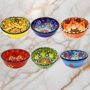 Pode incluir: Seis tigelas pequenas de cerâmica com padrões florais coloridos. As tigelas são de várias cores, incluindo amarelo, azul, laranja, vermelho, verde e azul claro.