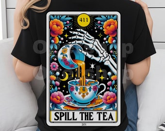 May include: A black t-shirt with a colorful tarot card design. The card features a skeleton hand pouring tea from a cup into another cup. The card is titled "Spill the Tea" with the numbers 411 and 201.