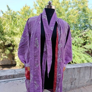 May include: A purple kantha quilted jacket with a white floral pattern and a red and orange pocket. The jacket has a tie closure and is made of a soft, lightweight fabric.