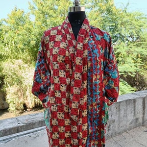 May include: A long, open-front kimono-style robe in red, blue, and beige. The robe features a patchwork design with geometric patterns and is displayed on a mannequin. The garment has long sleeves and a relaxed fit, suitable for layering.