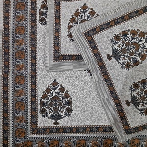 May include: A white cotton bed sheet with a brown and gray floral print. The sheet has a border with a repeating pattern of flowers and leaves.