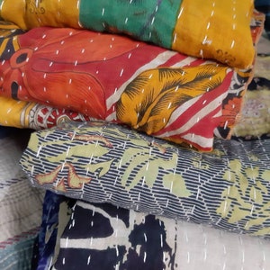 May include: A stack of colorful kantha quilts with intricate patterns and white stitching. The quilts are made from recycled saris and are a traditional Indian craft.