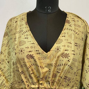 Op de afbeelding: Een beige kaftan met een V-hals en een strik in de taille. De kaftan is bedekt met een bruin en groen patroon van abstracte vormen en figuren.