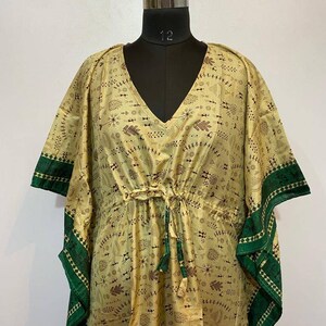 Op de afbeelding: Een lange, vloeiende kaftan met een V-hals en een trekkoord in de taille. De kaftan is gemaakt van een lichte, zijdeachtige stof en heeft een geometrische print in groen en bruin. De mouwen zijn kort en wijd, en de zoom is onregelmatig.