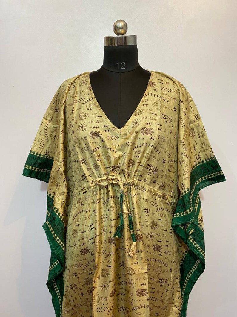 Op de afbeelding: Een lange, vloeiende kaftan met een V-hals en een trekkoord in de taille. De kaftan is gemaakt van een lichte, zijdeachtige stof en heeft een geometrische print in groen en bruin. De mouwen zijn kort en wijd, en de zoom is onregelmatig.