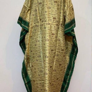 Op de afbeelding: Een lange, vloeiende kaftan met een groene bies. De kaftan is gemaakt van een lichte stof met een bruin en wit geometrisch patroon.