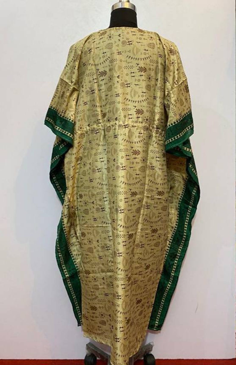 Op de afbeelding: Een lange, vloeiende kaftan met een groene bies. De kaftan is gemaakt van een lichte stof met een bruin en wit geometrisch patroon.