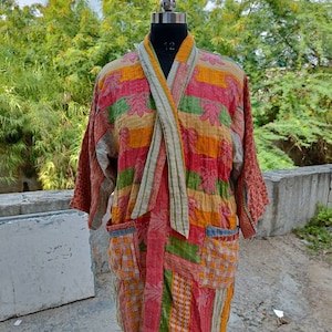 May include: A colorful patchwork kimono robe with a long, flowing design. The robe is made of a soft, quilted fabric and features a variety of colors, including red, orange, yellow, green, and blue. The robe has a tie closure at the front and two pockets on the sides.