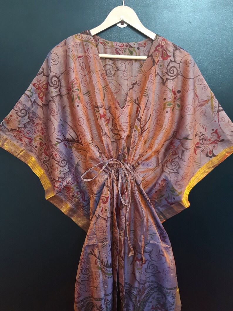 May include: A pink and brown patterned kaftan with gold trim. The kaftan has a V-neck and a drawstring waist.