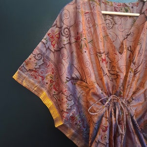 May include: A purple and gold kaftan with a floral pattern. The kaftan has a V-neck and a tie at the waist.