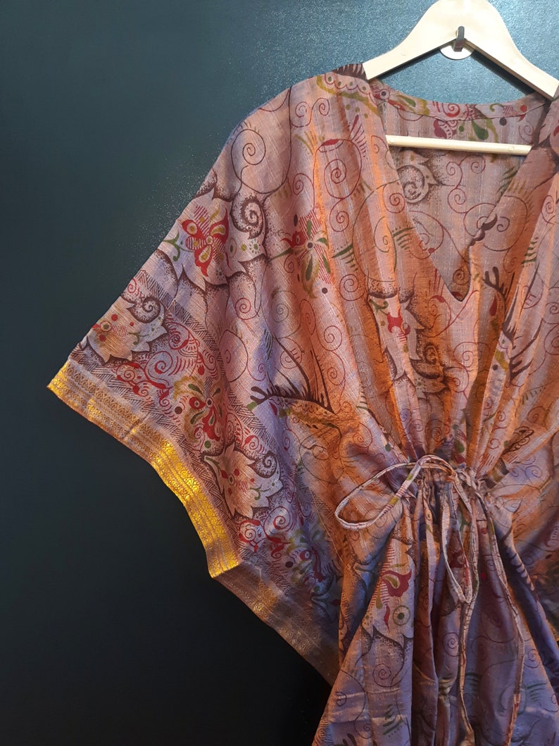 May include: A purple and gold kaftan with a floral pattern. The kaftan has a V-neck and a tie at the waist.