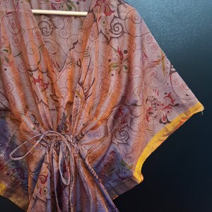 May include: A purple and orange patterned kaftan with gold trim. The kaftan has a V-neck and a drawstring waist.
