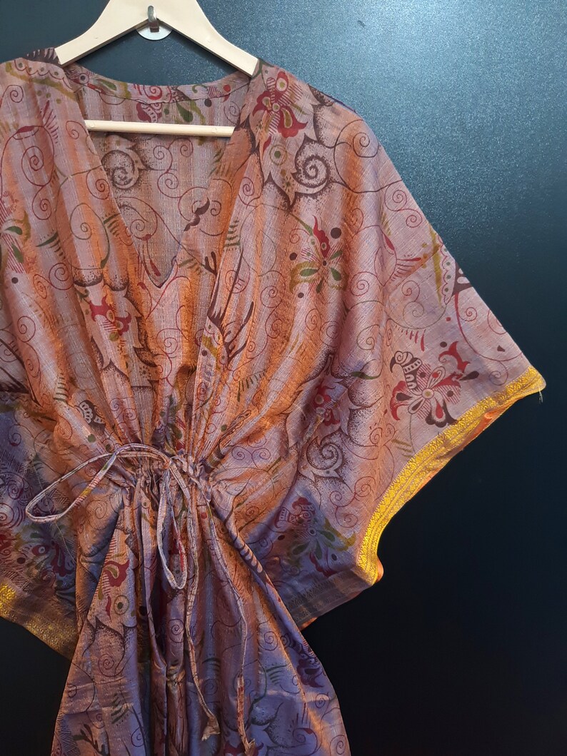 May include: A purple and orange patterned kaftan with gold trim. The kaftan has a V-neck and a drawstring waist.