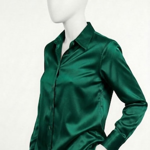 May include: A long-sleeved button-down shirt in a deep emerald green color with a smooth, satin-like finish. The shirt features a classic collar, a front button placket with matching green buttons, and cuffed sleeves, displayed on a mannequin.