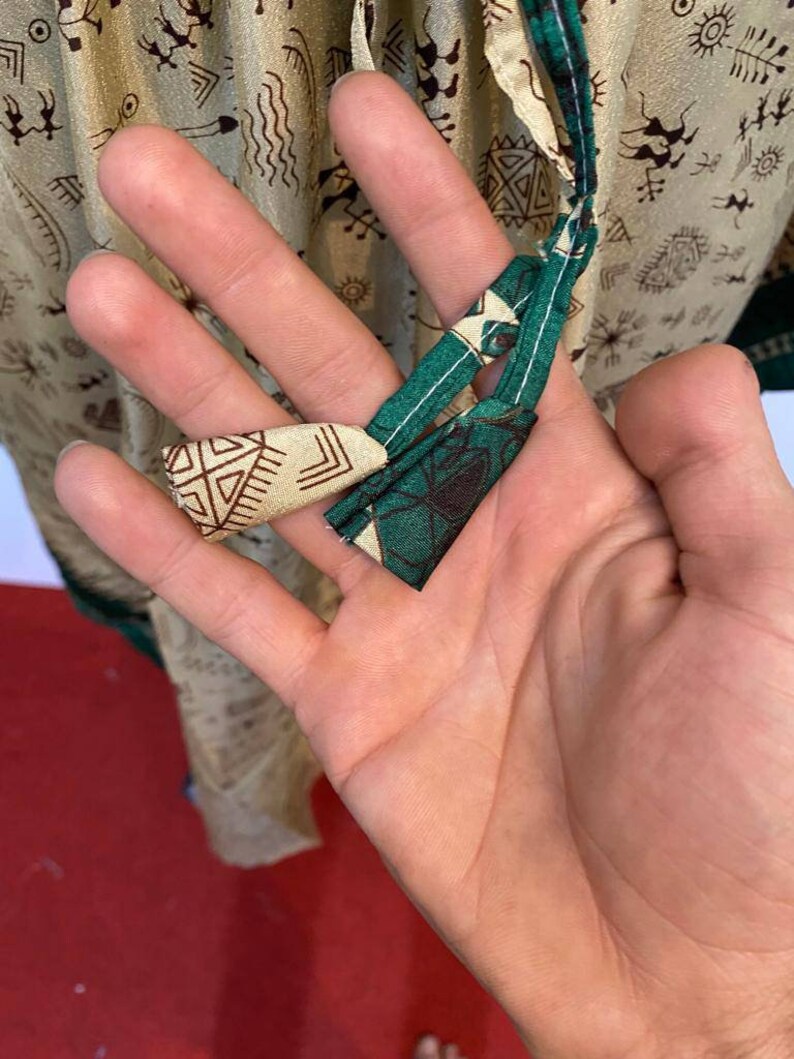 Op de afbeelding: Close-up van een groene en beige stoffen stropdas met een geometrisch patroon. De stropdas is in een knoop geknoopt en wordt vastgehouden door een hand.