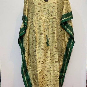 Op de afbeelding: Een lange, beige kaftan met een groene bies en een geometrisch patroon. De kaftan heeft een V-hals en een trekkoord in de taille.