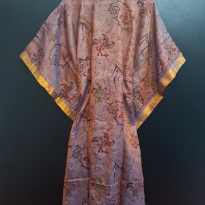 May include: A long, flowing, pink silk robe with a floral pattern and gold trim. The robe has a wide, open neckline and long sleeves.